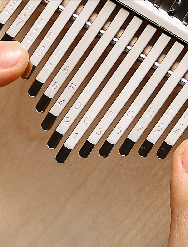 Detailed view of a 34-key chromatic kalimba with a double-layer tine arrangement, showing the pitch engravings on the metal keys and the ergonomic curved design of the wooden body.