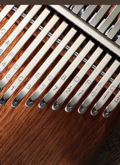 Top-down view of a handcrafted kalimba showing its ergonomic curved body, unique brand logo inlay, and neatly arranged metal keys labeled with musical notes and numbers.