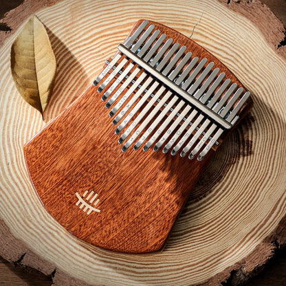 A 17-key solid wood kalimba by Moral Gain, resting on a circular wood slab base, featuring deep brown wood grain and polished metal tines with engraved note markings.