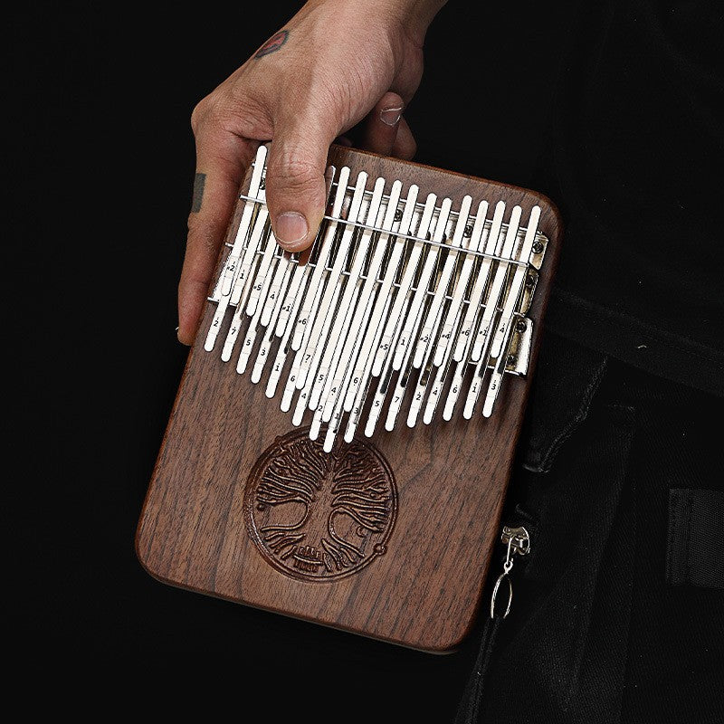 A 21-key walnut kalimba thumb piano featuring an intricate "Tree of Life" engraving on the solid wood body, being held by a person.