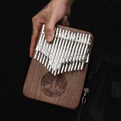 A 21-key walnut kalimba thumb piano featuring an intricate "Tree of Life" engraving on the solid wood body, being held by a person.